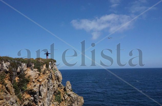Chico al filo de un acantilado imitando el vuelo de un pájaro